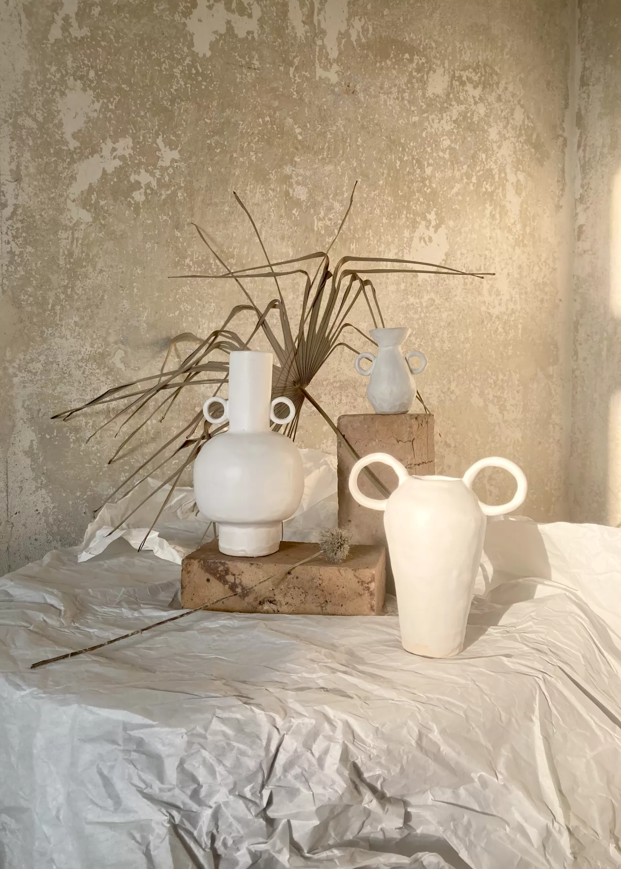 Białe ceramiczne wazony ustawione w ciepłym świetle na tle surowej ściany